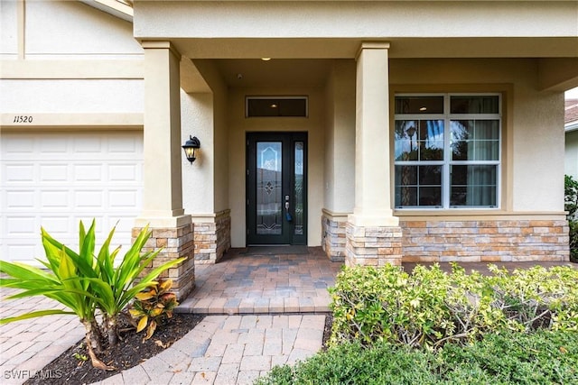 entrance to property featuring a garage, stone siding, and stucco siding