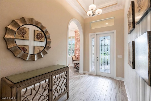 entrance foyer featuring baseboards, ornamental molding, an inviting chandelier, a tray ceiling, and light wood-style floors