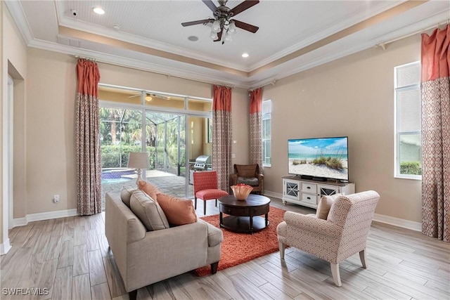 living room with a wealth of natural light, a tray ceiling, crown molding, and light wood finished floors