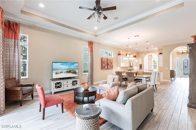 living room with arched walkways, a tray ceiling, crown molding, and light wood-style floors