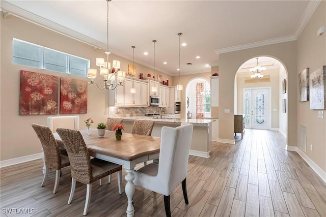 dining space featuring light wood-type flooring, baseboards, arched walkways, and a notable chandelier