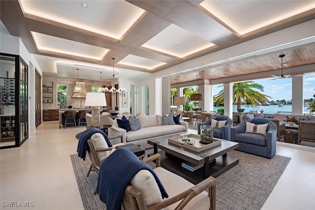 living room featuring a water view, coffered ceiling, and a chandelier