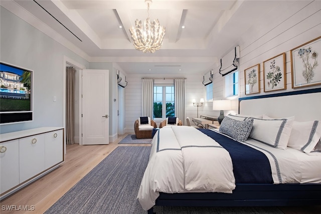 bedroom with a chandelier, a raised ceiling, and light wood-type flooring