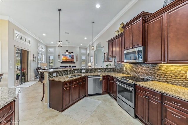 kitchen featuring sink, appliances with stainless steel finishes, light stone counters, decorative light fixtures, and kitchen peninsula