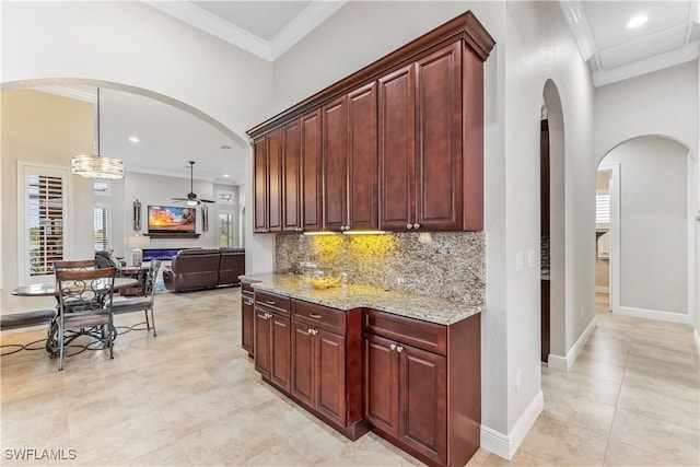 kitchen with decorative light fixtures, tasteful backsplash, ornamental molding, ceiling fan, and light stone counters