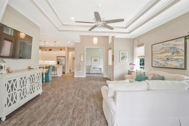 living room featuring wood-type flooring, ornamental molding, a raised ceiling, and ceiling fan