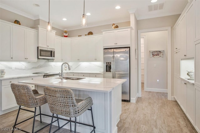 kitchen featuring sink, white cabinetry, pendant lighting, stainless steel appliances, and a kitchen island with sink