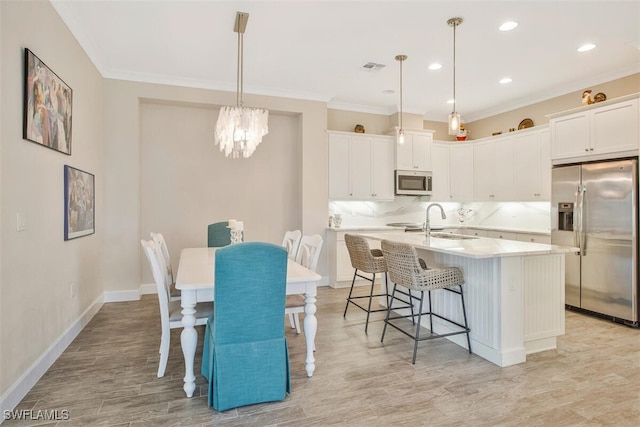 kitchen with appliances with stainless steel finishes, pendant lighting, white cabinetry, a breakfast bar area, and a kitchen island with sink