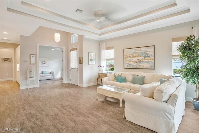 living room with ceiling fan, a tray ceiling, and light hardwood / wood-style flooring