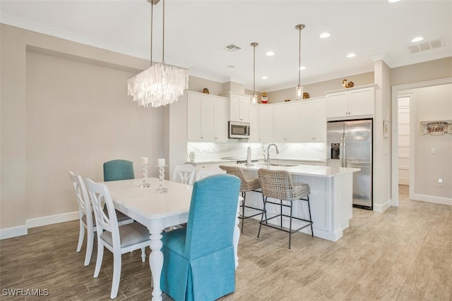 dining area with crown molding, a notable chandelier, sink, and light wood-type flooring