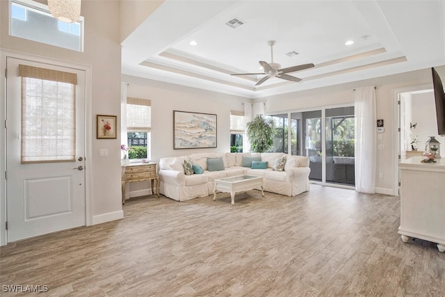 living room featuring a raised ceiling, plenty of natural light, and light wood-type flooring