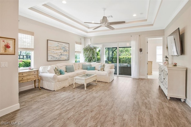 living room featuring a tray ceiling, ornamental molding, and light wood-type flooring