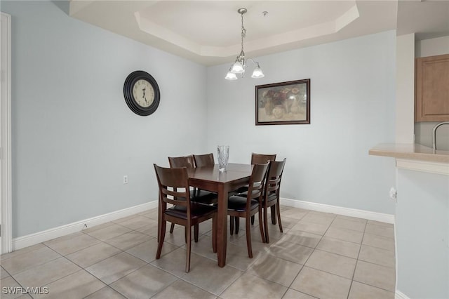 tiled dining space with an inviting chandelier and a tray ceiling