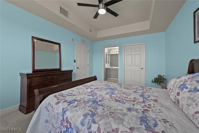 bedroom featuring ceiling fan, light colored carpet, ensuite bathroom, and a tray ceiling