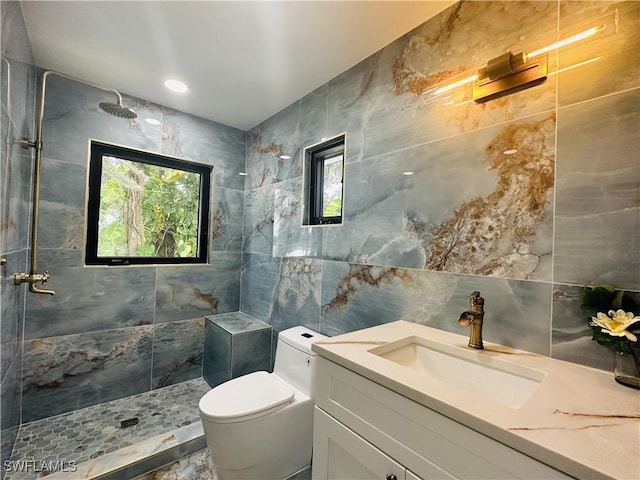 bathroom featuring a tile shower, tile walls, vanity, and toilet