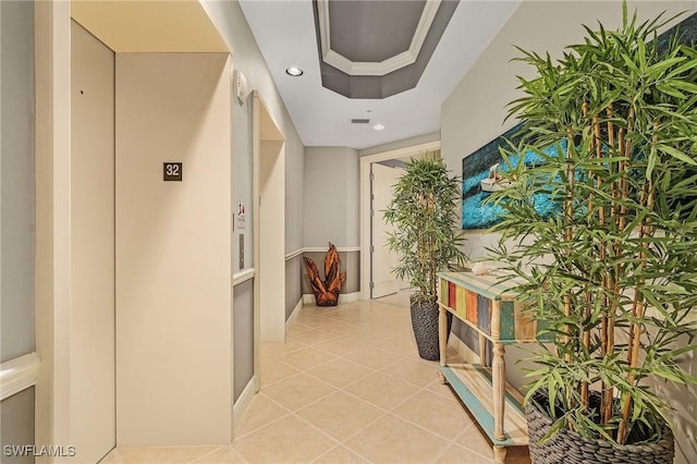 hallway featuring elevator, a tray ceiling, and light tile patterned floors