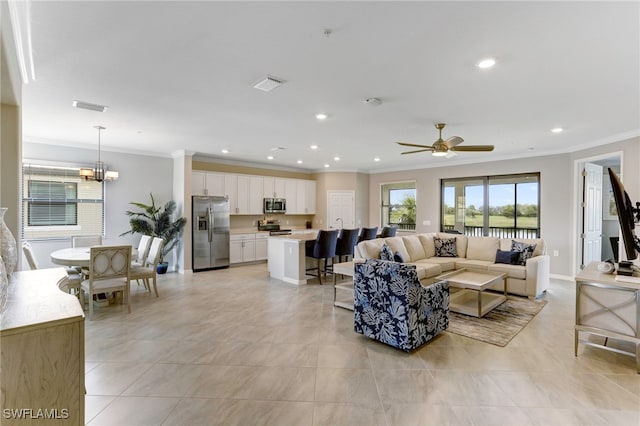 tiled living room with ceiling fan with notable chandelier and ornamental molding