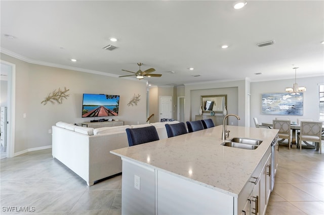 kitchen with decorative light fixtures, sink, crown molding, light stone countertops, and a center island with sink