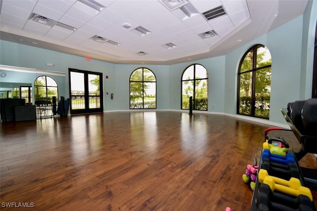 exercise area featuring dark wood-type flooring, a towering ceiling, a tray ceiling, and a paneled ceiling