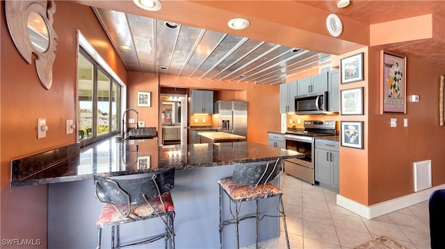 kitchen featuring sink, a breakfast bar, appliances with stainless steel finishes, light tile patterned flooring, and dark stone counters