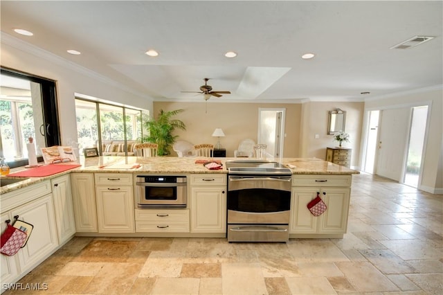 kitchen with ornamental molding, ceiling fan, light stone counters, stainless steel appliances, and cream cabinetry