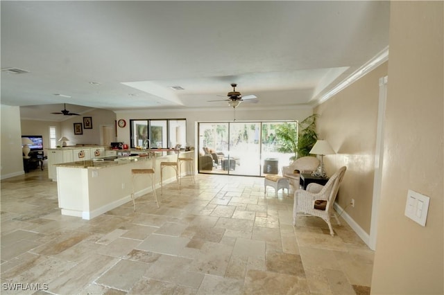 kitchen featuring light stone counters, ceiling fan, crown molding, and a breakfast bar