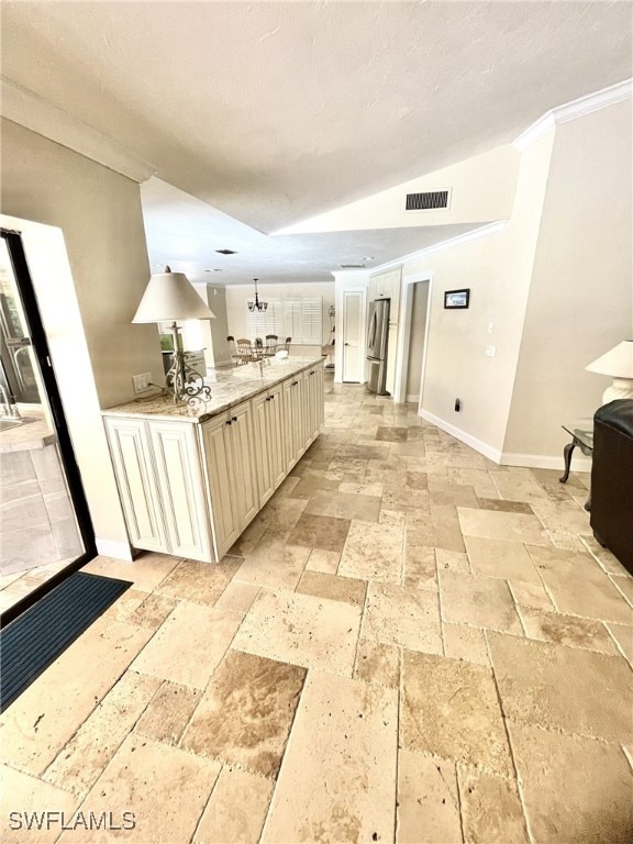 kitchen featuring stainless steel refrigerator, ornamental molding, light stone counters, and cream cabinetry