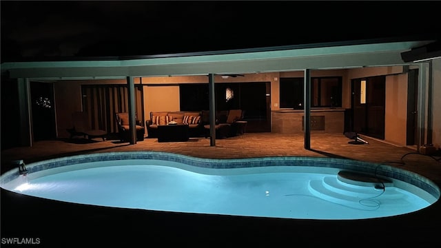 pool at night featuring a patio, an outdoor hangout area, and an outdoor bar