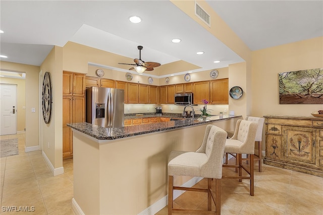 kitchen featuring ceiling fan, appliances with stainless steel finishes, dark stone countertops, a kitchen bar, and kitchen peninsula