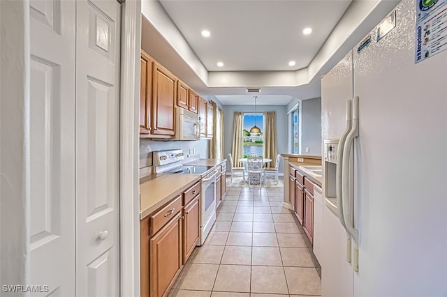 kitchen with sink, light tile patterned floors, white appliances, decorative light fixtures, and a raised ceiling