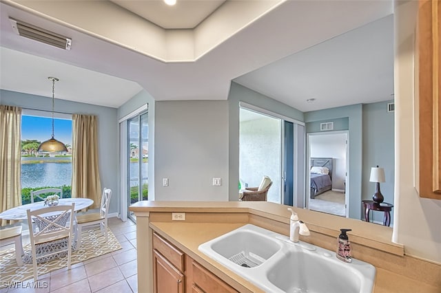 kitchen featuring pendant lighting, sink, light tile patterned floors, and a water view