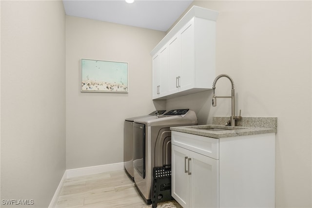 washroom featuring cabinets, sink, independent washer and dryer, and light hardwood / wood-style flooring