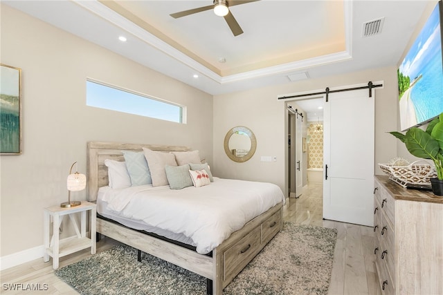 bedroom featuring a tray ceiling, light hardwood / wood-style flooring, a barn door, and ceiling fan