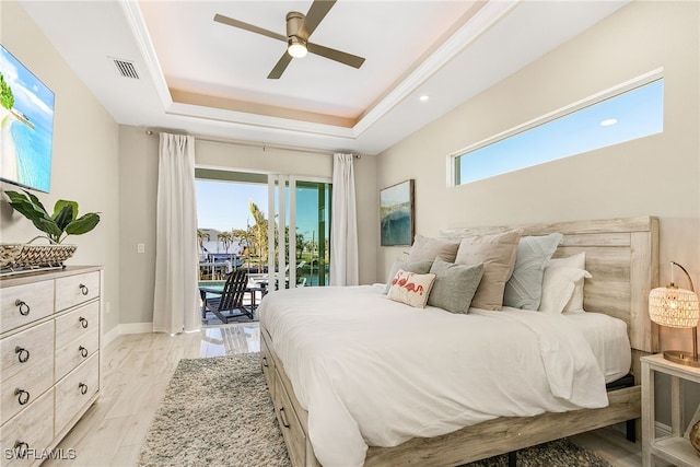 bedroom featuring multiple windows, access to exterior, light hardwood / wood-style floors, and a raised ceiling