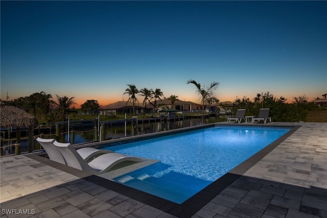 pool at dusk featuring a water view and a patio area