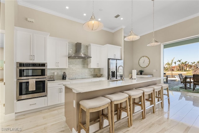 kitchen featuring pendant lighting, white cabinetry, sink, a center island with sink, and wall chimney exhaust hood