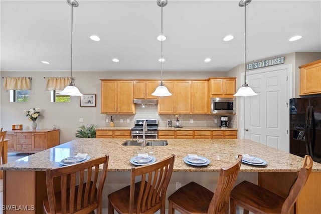 kitchen with sink, appliances with stainless steel finishes, a kitchen island with sink, backsplash, and decorative light fixtures