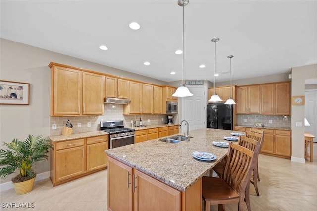 kitchen with sink, appliances with stainless steel finishes, a kitchen breakfast bar, light stone countertops, and an island with sink