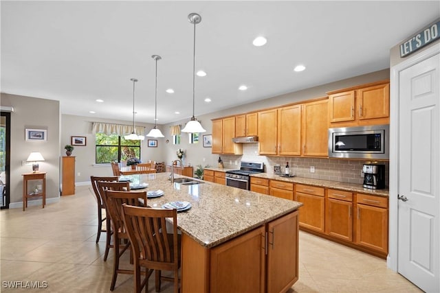 kitchen featuring sink, decorative light fixtures, stainless steel appliances, and an island with sink