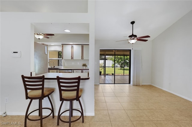 kitchen featuring light tile patterned flooring, sink, stainless steel fridge, ceiling fan, and kitchen peninsula