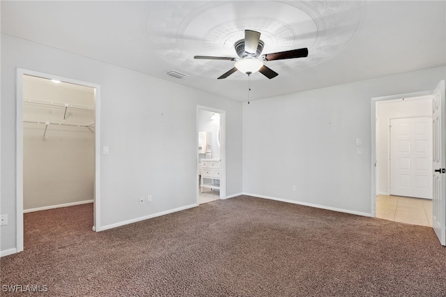 unfurnished bedroom featuring ensuite bathroom, a spacious closet, a closet, ceiling fan, and carpet