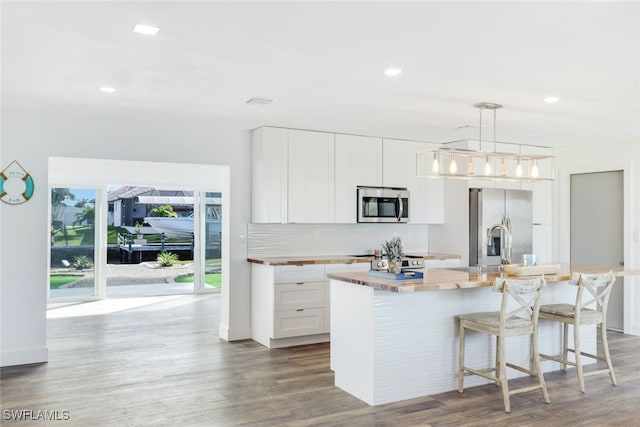 kitchen with hanging light fixtures, a kitchen breakfast bar, an island with sink, stainless steel appliances, and white cabinets