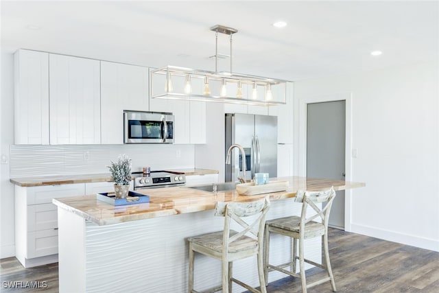 kitchen with hanging light fixtures, a center island with sink, white cabinets, and appliances with stainless steel finishes