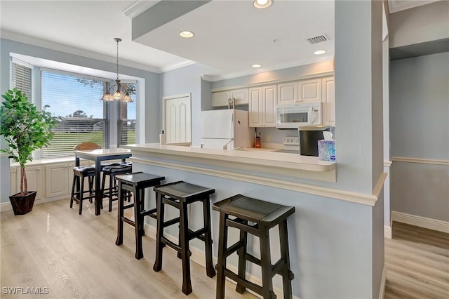 kitchen with pendant lighting, a kitchen bar, ornamental molding, light hardwood / wood-style floors, and white appliances