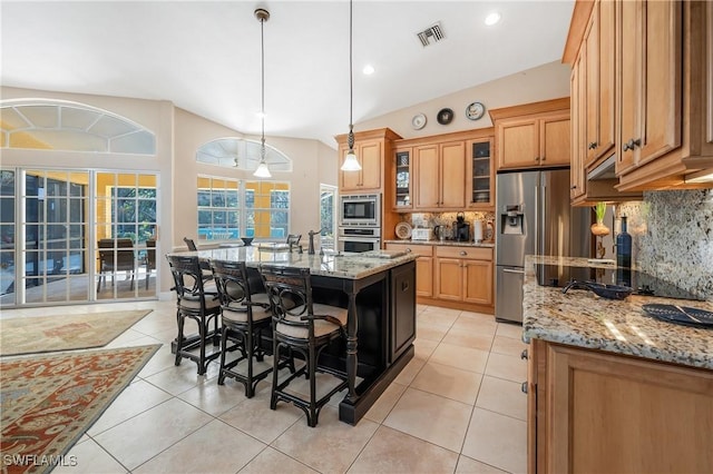 kitchen with a breakfast bar area, light stone counters, hanging light fixtures, an island with sink, and stainless steel appliances