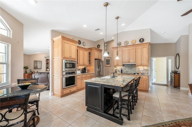 kitchen with appliances with stainless steel finishes, sink, hanging light fixtures, a kitchen island with sink, and light stone countertops