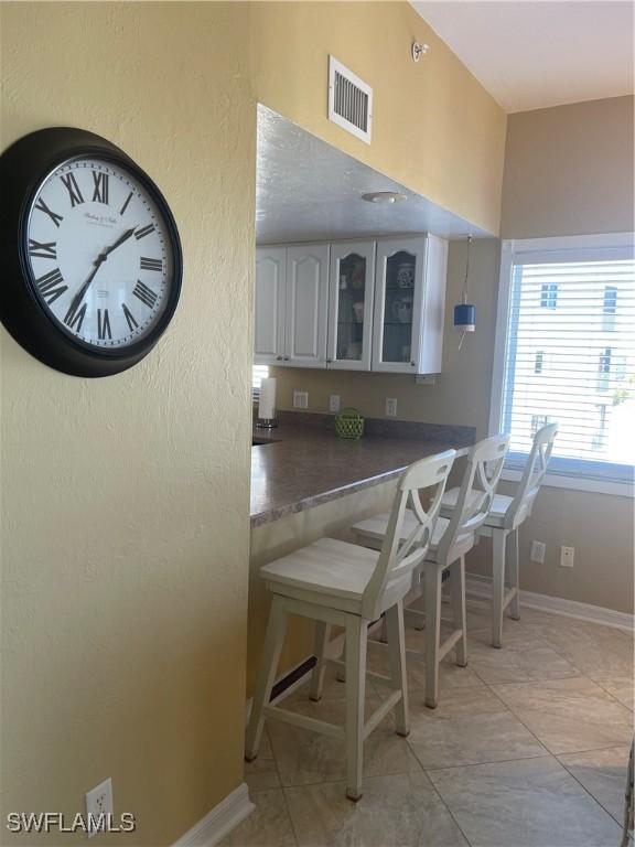 kitchen featuring white cabinetry, light tile patterned floors, kitchen peninsula, and a kitchen bar