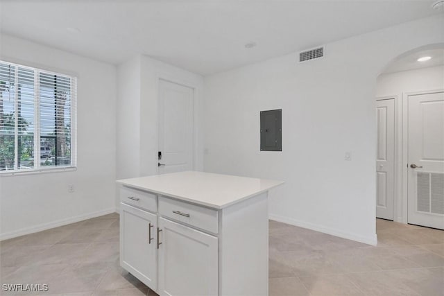 kitchen featuring electric panel, light tile patterned floors, a kitchen island, and white cabinets