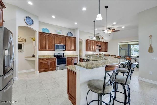 kitchen with sink, hanging light fixtures, an island with sink, stainless steel appliances, and light stone countertops