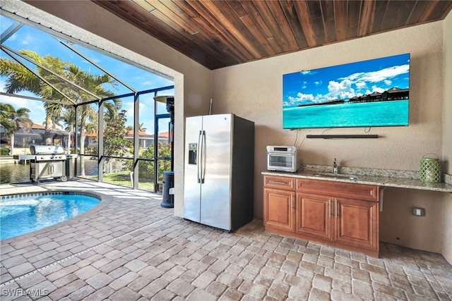 kitchen with stainless steel fridge with ice dispenser, wooden ceiling, sink, and light stone countertops